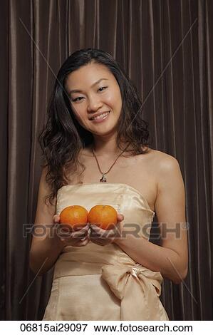 Stock Photo - Chinese woman holding two oranges and smiling. Fotosearch