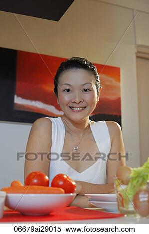 Stock Photography - Chinese woman sitting at table with vegetables in front of her. Fotosearch