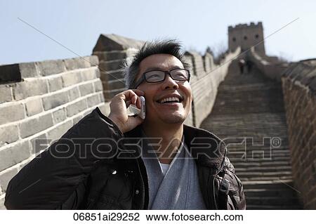 Stock Image - Man talking on phone while standing on the Great Wall, China. Fotosearch