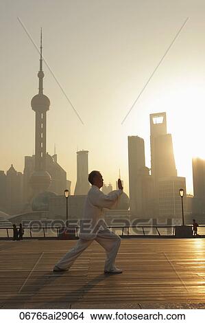 Picture - Mature man doing tai chi on Bund at sunrise with Shanghai skyline in background. Fotosearch
