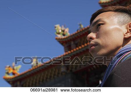 Stock Image - Profile of Man looking off with Buddhist temple in background. Fotosearch