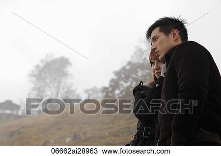 Stock Image - Profile of young couple wearing coats hugging outdoors. Fotosearch