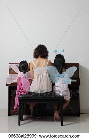 Stock Photo - Rear view of mother sitting with daughters at piano. Fotosearch