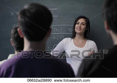 Stock Image - Rear view of students watching teacher at chalk baord. Fotosearch