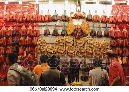 Picture - Small group of people looking at dried meat hanging in a market. Fotosearch