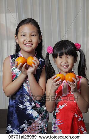 Stock Photo - Two young Chinese girls holding oranges and smiling. Fotosearch