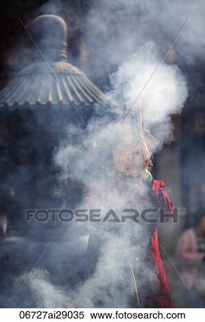Stock Photography - Woman praying with incense surrounded by smoke in front of Buddhist temple, China. Fotosearch
