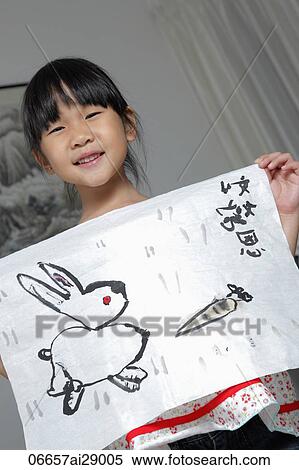 Stock Photography - Young Chinese girl smiling holding up picture of rabbit. Fotosearch