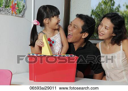 Stock Image - Young girl putting away toys with her parents and laughing. Fotosearch