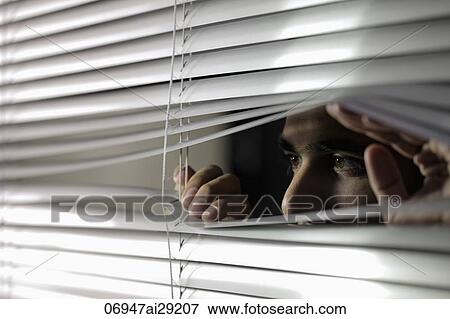 Stock Photo - Young man looking through silver blinds.. Fotosearch