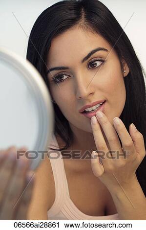 Stock Image - Young woman looking at mirror, touching her lips. Fotosearch
