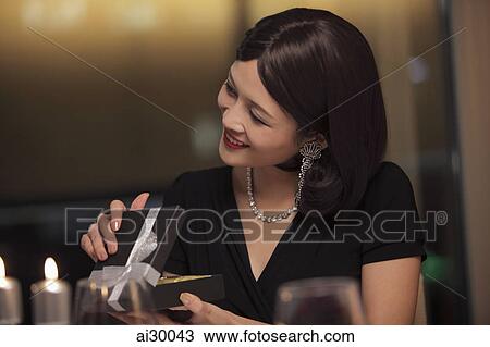Stock Image - A young dressed up woman opening a present. Fotosearch