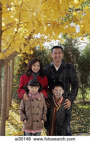 Family of four wearing coats standing under a tree with yellow leaves View Large Photo Image Stock Photo - Family of four wearing coats standing under a tree with yellow leaves. Fotosearch