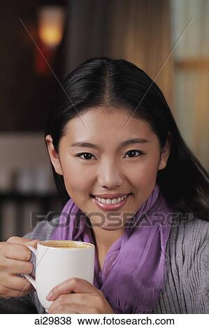 Stock Photo - Head shot of young woman holding coffee cup and smiling. Fotosearch