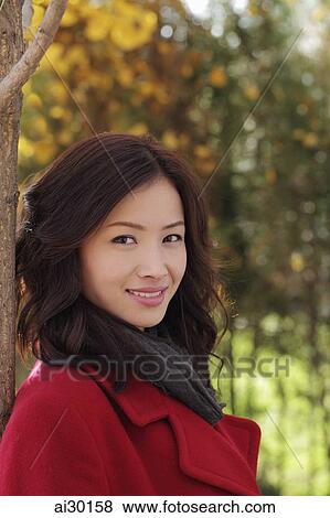 Head shot of young woman in a red coat under a tree View Large Photo Image Stock Photo - Head shot of young woman in a red coat under a tree. Fotosearch