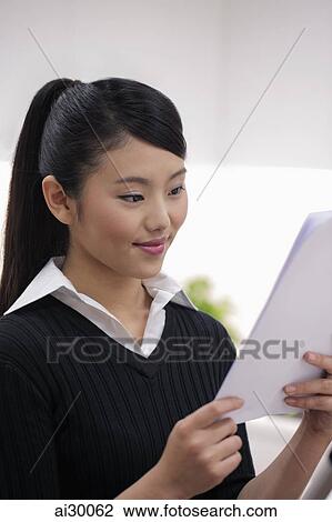 Stock Image - Head shot of young woman looking at paper. Fotosearch