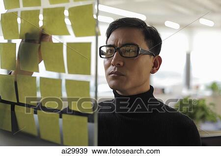 man wearing glasses looking at stick on notes View Large Photo Image Stock Photo - man wearing glasses looking at stick on notes. Fotosearch