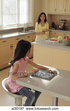 Mother watching her daughter play on a digital tablet as she cooks View Large Photo Image Stock Photo - Mother watching her daughter play on a digital tablet as she cooks. Fotosearch