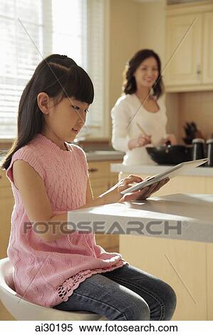 Mother watching her daughter play on a digital tablet as she cooks View Large Photo Image Stock Photography - Mother watching her daughter play on a digital tablet as she cooks. Fotosearch