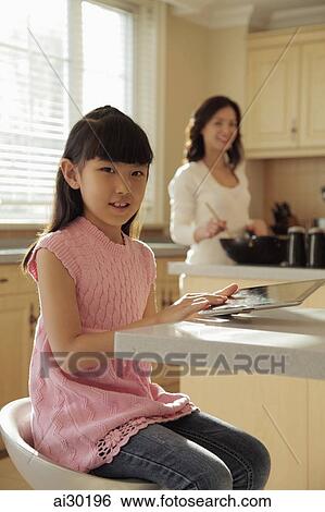 Mother watching her young daughter play on a digital tablet as she cooks View Large Photo Image Stock Photograph - Mother watching her young daughter play on a digital tablet as she cooks. Fotosearch