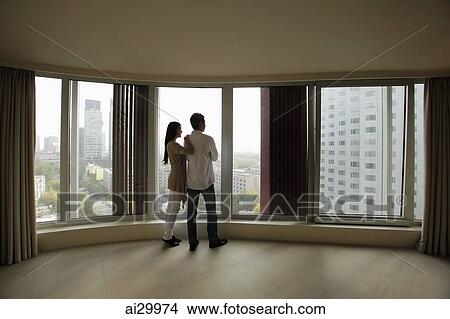 Rear view of young couple looking out large windows of condo View Large Photo Image Picture - Rear view of young couple looking out large windows of condo. Fotosearch