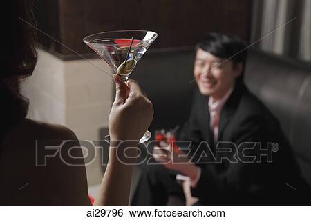 Rear view of young woman holding a drink looking at a man View Large Photo Image Stock Photograph - Rear view of young woman holding a drink looking at a man. Fotosearch