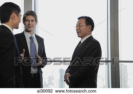 Stock Image - Three businessmen talking together. Fotosearch