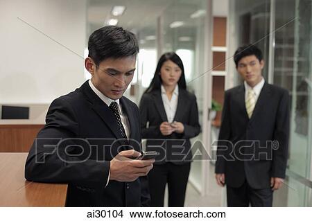 Three businesspeople standing in office, one texting on a phone View Large Photo Image Picture - Three businesspeople standing in office, one texting on a phone. Fotosearch