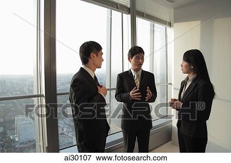 Three businesspeople talking in front of a window View Large Photo Image Stock Photo - Three businesspeople talking in front of a window. Fotosearch