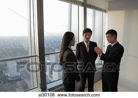 Three businesspeople talking in front of a window View Large Photo Image Stock Photo - Three businesspeople talking in front of a window. Fotosearch