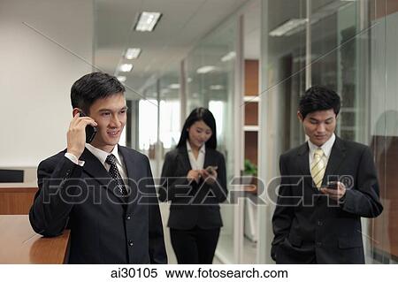 Stock Photography - Three businesspeople using their phones in the office. Fotosearch