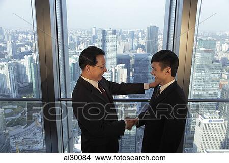 Picture - Two men shaking hands in front of window with a view of the city of Beijing. Fotosearch