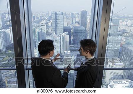 Stock Photograph - Two men talking in front of window with a view of the city of Beijing. Fotosearch