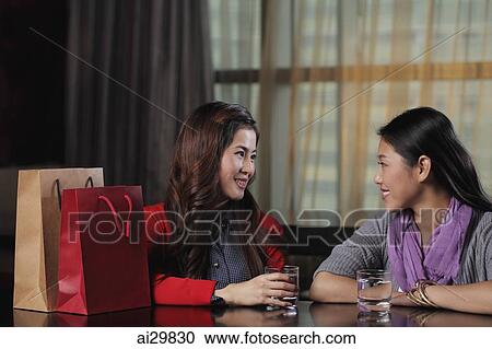 Two young woman talking at a cafe with shopping bags View Large Photo Image Stock Image - Two young woman talking at a cafe with shopping bags. Fotosearch