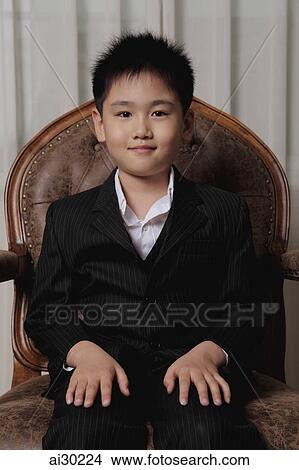Picture - Young boy wearing a suit sitting on a chair. Fotosearch