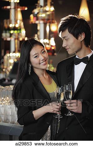 Stock Image - Young couple dressed up toasting with champagne glasses. Fotosearch