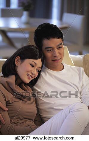 Young couple sitting on sofa together View Large Photo Image Stock Photo - Young couple sitting on sofa together. Fotosearch