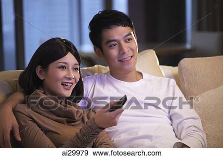 Stock Photo - Young couple sitting on sofa watching TV together. Fotosearch