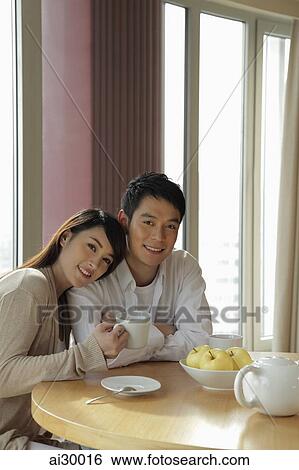 Young couple sitting together in their home View Large Photo Image Stock Photograph - Young couple sitting together in their home. Fotosearch