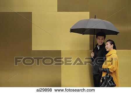 Young couple walking on street holding an umbrella View Large Photo Image Stock Photo - Young couple walking on street holding an umbrella. Fotosearch