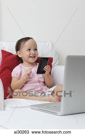 Young girl holding phone and playing with laptop View Large Photo Image Stock Image - Young girl holding phone and playing with laptop. Fotosearch