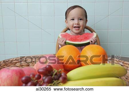 Stock Photography - Young girl holding watermelon with a bowl of fruit in front of her. Fotosearch