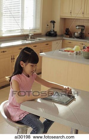 Young girl plays on a digital tablet computer in the kitchen View Large Photo Image Stock Photo - Young girl plays on a digital tablet computer in the kitchen. Fotosearch
