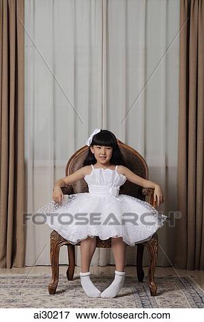 Stock Photo - Young girl wearing white dress sitting in nice chair smiling. Fotosearch