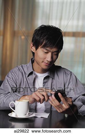 Young man sitting at a table texting on phone View Large Photo Image Stock Image - Young man sitting at a table texting on phone. Fotosearch