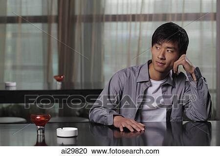 Young man sitting at a table thinking View Large Photo Image Stock Image - Young man sitting at a table thinking. Fotosearch