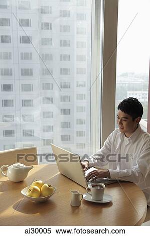Stock Photography - Young man sitting at a table working on laptop computer. Fotosearch
