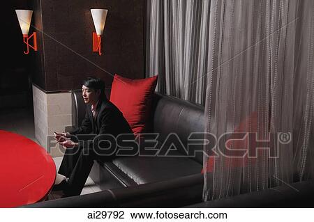 Young man sitting in a club holding a drink View Large Photo Image Stock Image - Young man sitting in a club holding a drink. Fotosearch