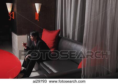 Stock Image - Young man sitting in a club holding a drink. Fotosearch