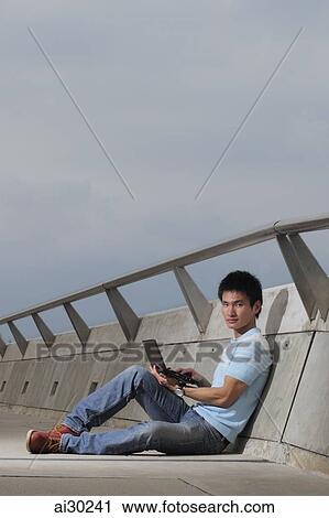Young man sitting on ground working on laptop View Large Photo Image Stock Image - Young man sitting on ground working on laptop. Fotosearch